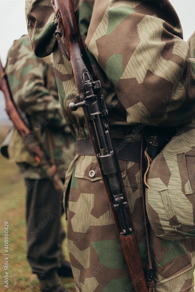 A man in a soldier's co-ornate uniform with a rifle carbine on his shoulder during a reconstruction of military action A man in a soldier's co-ornate uniform with a rifle carbine on his shoulder during a reconstruction of military action
