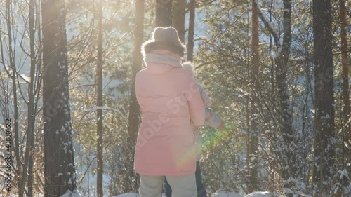 Young Woman with Child Girl Having Fun in Winter Pine Forest in Sunny Freezing Day. Slow Motion. Concept of Happy Childhood, Winter Family Activities, People and Lifestyle Concept photo