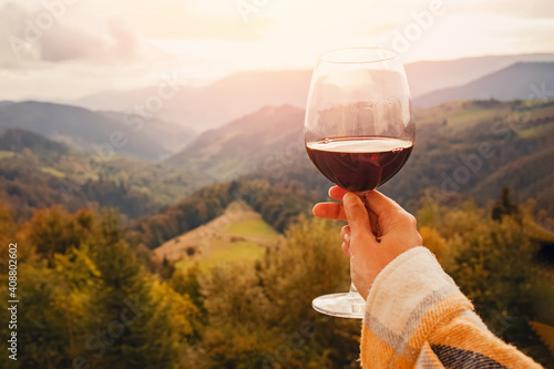 Woman's hand holding a glass of red wine with a mountain view.