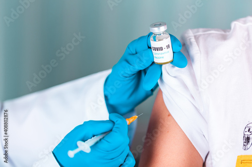 Doctor or nurse in uniform and gloves wearing face mask protective in lab making an injecion holding vaccine bottle with COVID-19 Coronovirus vaccine label