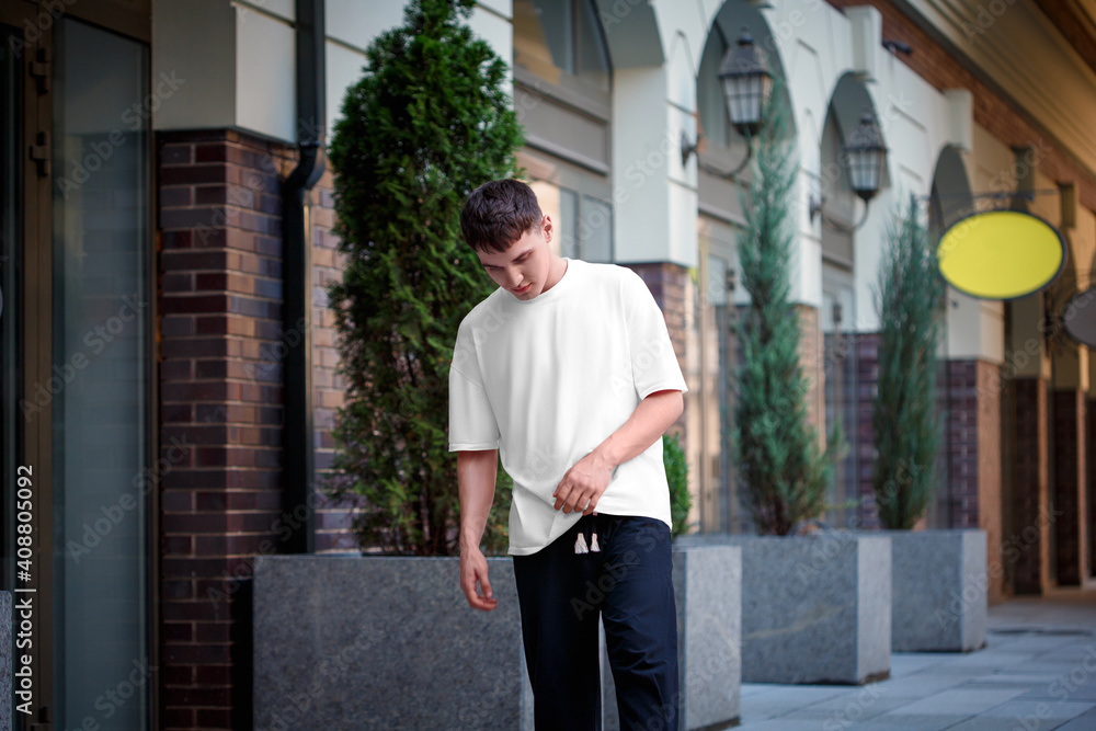 Male white t-shirt template on guy posing against blurred street background, urban style clothing for design presentation. Male white t-shirt template on guy posing against blurred street background, urban style clothing for design presentation.