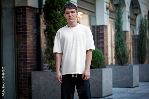 Mockup of a white T-shirt on a guy in dark pants, stylish urban style clothes on a blurred street background. © olegphotor
