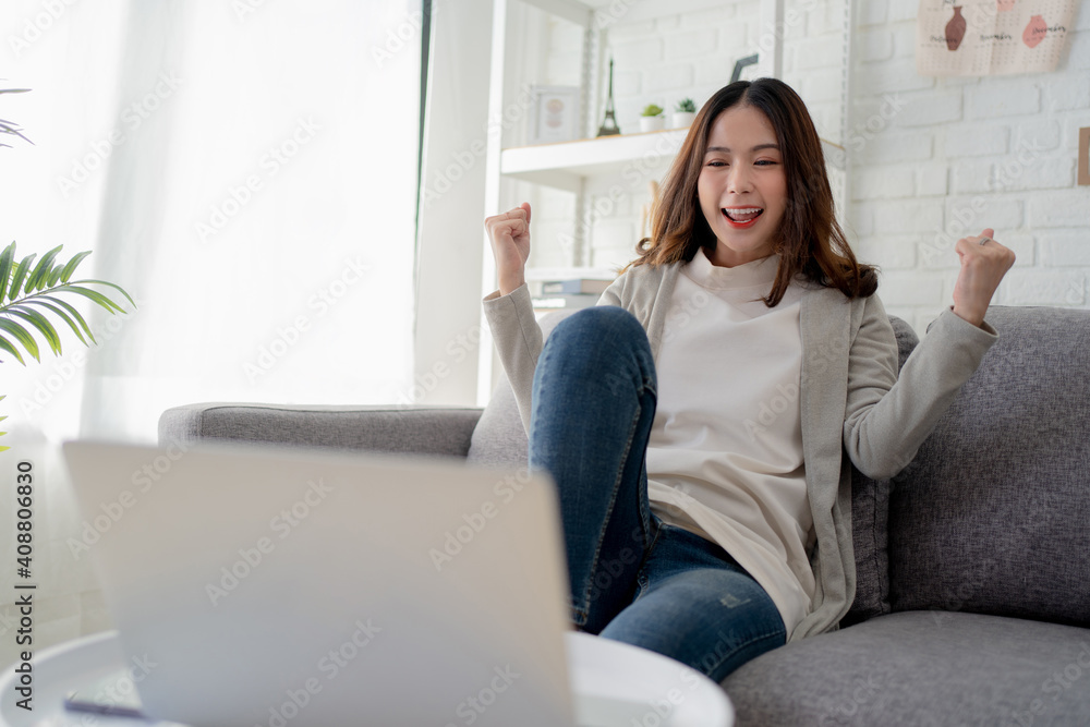Young Asian woman are having fun and excitement sitting on the sofa. She was reading the news on a laptop at home. Young Asian woman are having fun and excitement sitting on the sofa. She was reading the news on a laptop at home.