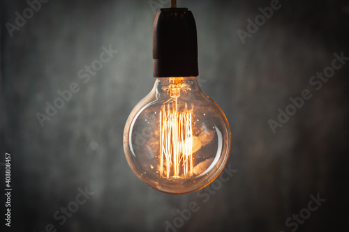 incandescent light bulb with tungsten filaments on old rustic grey concrete wall background. Save the energy