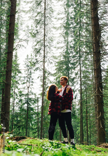 Vertical photo, romantic couple man and woman while walking in a mountain forest on a climb up the mountain stand in the arms of moss on a background of beautiful trees