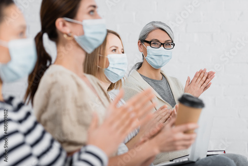 asian businesswoman in medical mask applauding with colleagues during seminar