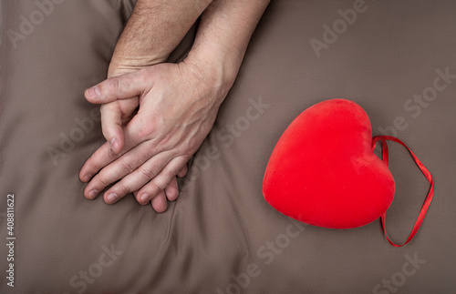LGBT concept. Men holding hands with passion on the bed near red heart. Hands of couple of homosexual men on brown pillow. Same sex love. Gay relationships. Valentines card for gays