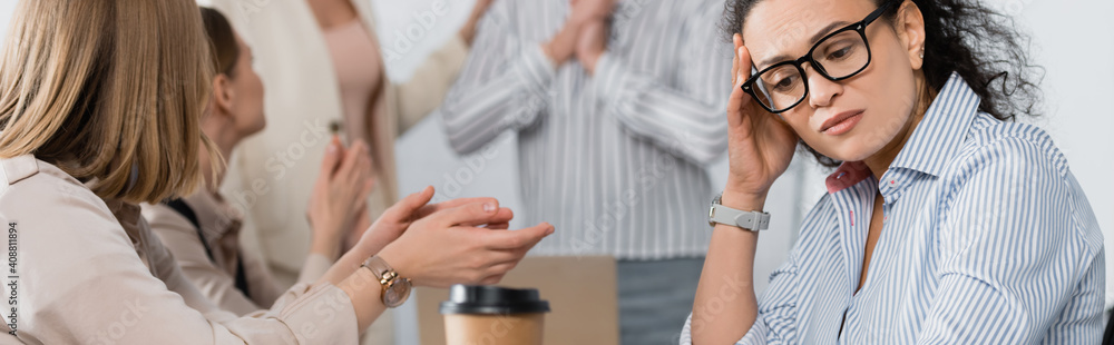 African american businesswoman looking at paper cup near coworkers on blurred background, banner