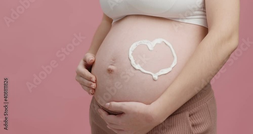 Wallpaper Mural Healthy prenatal cosmetics. Close up of big pregnant belly with cream heart on it, pink studio background Torontodigital.ca