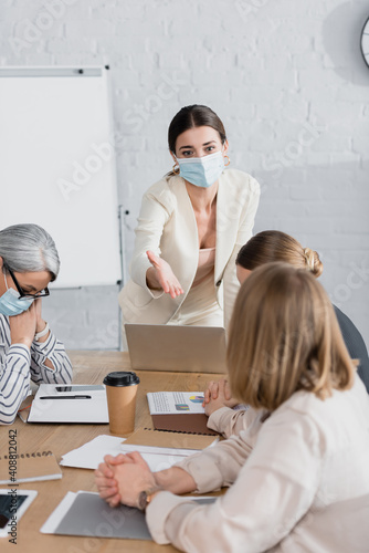 team leader in medical mask pointing with hand at businesswoman during seminar