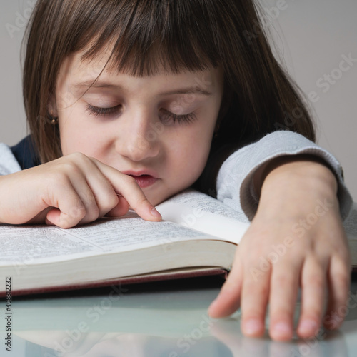 Tired and exhausted young beautiful child girl reading the book Close up.