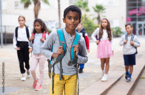 Portrait of african american boy standing near school, children on background