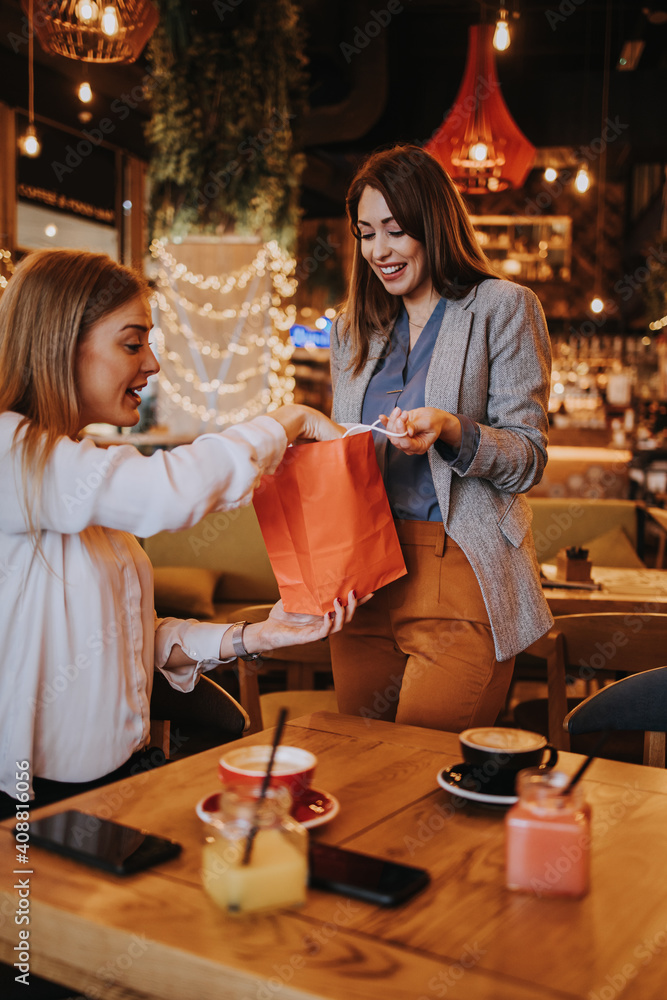 Two best friends meet in a nice restaurant or coffee bar. One prepares a surprise for the other and gives her a birthday present. Happy young people. Two best friends meet in a nice restaurant or coffee bar. One prepares a surprise for the other and gives her a birthday present. Happy young people.