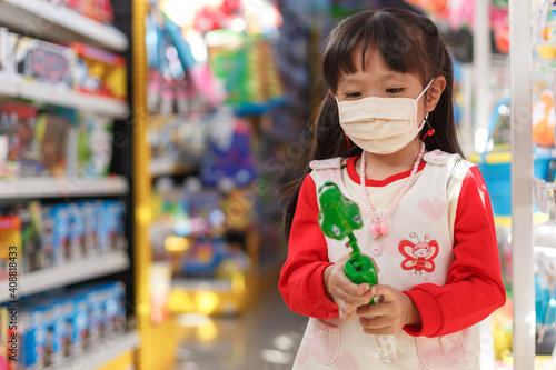 girl in sanitary face mask shopping at toy store. Child wearing protective mask against coronavirus.