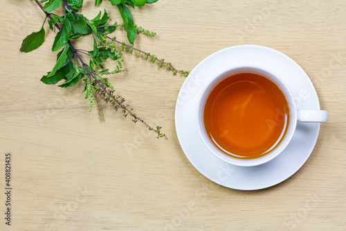 Tulsi or holy basil tea in white cup with fresh tulsi branch on wooden background top view. Ayurvedic medicine in India.