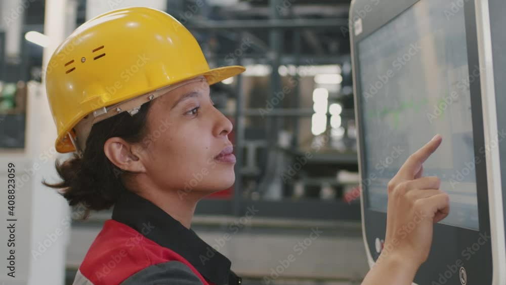 Slow-motion close-up of female mixed race engineer setting parameters for machinery equipment using touchscreen working at factory Slow-motion close-up of female mixed race engineer setting parameters for machinery equipment using touchscreen working at factory