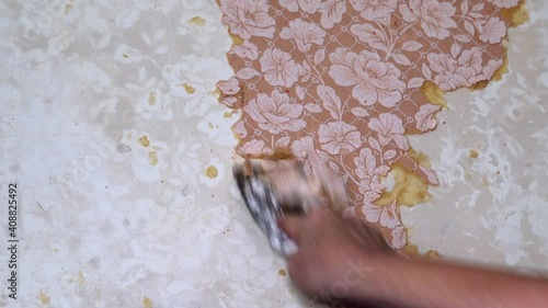 female hand strips wallpaper from the wall of a room