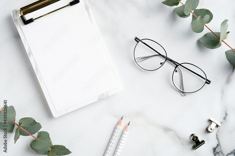 Elegant feminine home office desk with paper clipboard, glasses, eucalyptus branches on marble background. Minimal style workspace. Flat lay, top view. Elegant feminine home office desk with paper clipboard, glasses, eucalyptus branches on marble background. Minimal style workspace. Flat lay, top view.