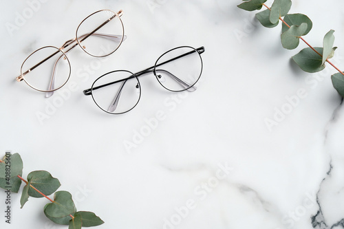 Woman's eyeglasses and eucalyptus branches on marble background. Flat lay, top view.