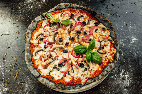 A top view of appetizing pizza with black dough and various vegetables