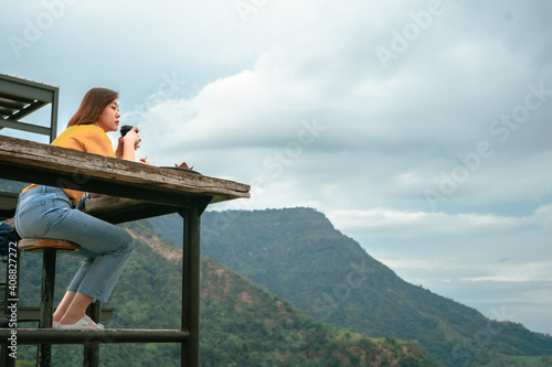 asian woman solo traveler drink coffee with relax at outdoor coffeeshop with mountain background