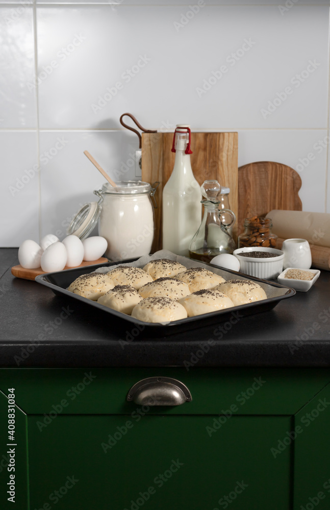 raw homemade yeast buns are ready for baking on the table with ingredients: milk, flour, eggs, oil raw homemade yeast buns are ready for baking on the table with ingredients: milk, flour, eggs, oil