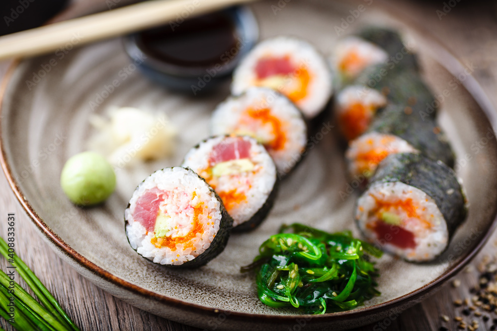 Sushi maki rolls with tuna, flying fish caviar, crab, avocado on a plate with chopsticks, soy sauce, wasabi and ginger. Japanese traditional food closeup served for lunch in modern gourmet restaurant Sushi maki rolls with tuna, flying fish caviar, crab, avocado on a plate with chopsticks, soy sauce, wasabi and ginger. Japanese traditional food closeup served for lunch in modern gourmet restaurant