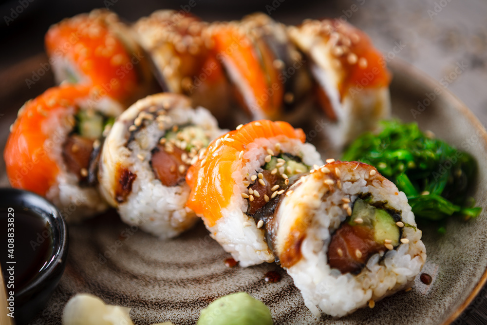 Sushi maki rolls with salmon, eel, avocado, cucumber on a plate with chopsticks, soy sauce, wasabi and ginger. Japanese traditional fish food closeup served for lunch in modern gourmet restaurant Sushi maki rolls with salmon, eel, avocado, cucumber on a plate with chopsticks, soy sauce, wasabi and ginger. Japanese traditional fish food closeup served for lunch in modern gourmet restaurant