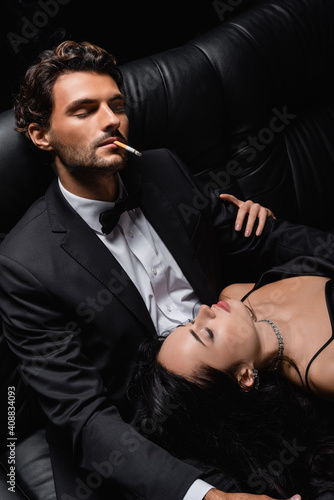 man with closed eyes smoking cigarette near sexy woman lying on his laps © LIGHTFIELD STUDIOS