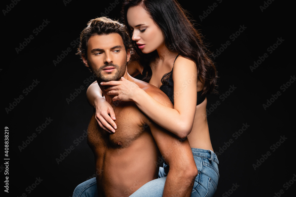 shirtless muscular man piggybacking passionate woman touching his face isolated on black shirtless muscular man piggybacking passionate woman touching his face isolated on black
