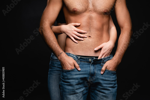 partial view of seductive woman hugging shirtless man with muscular torso isolated on black