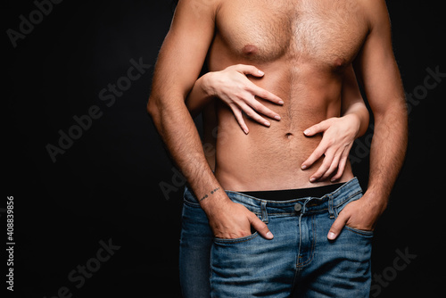 partial view of woman embracing muscular torso of sexy man isolated on black