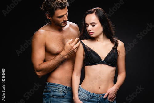passionate shirtless man touching bra of sensual brunette woman isolated on black