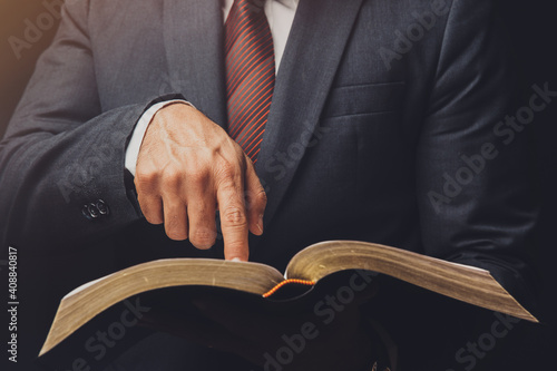 Konstfotografi man in suit pointing a text on an open bible on a black background