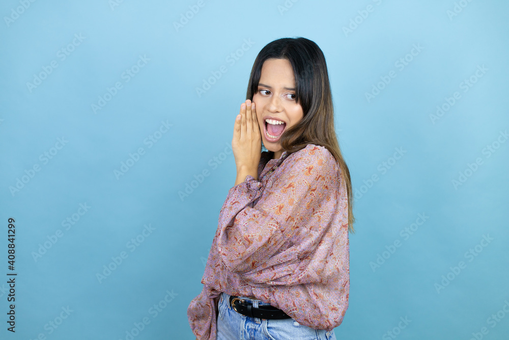 Beautiful latin woman wearing a pink shirt over blue isolated background with hand on mouth telling secret rumor, whispering malicious talk conversation Beautiful latin woman wearing a pink shirt over blue isolated background with hand on mouth telling secret rumor, whispering malicious talk conversation
