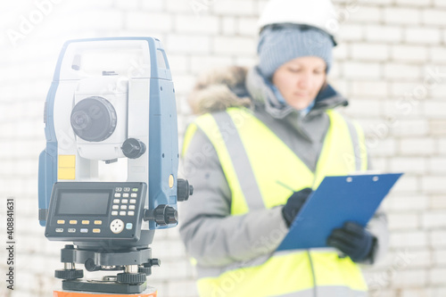 a female engineer surveyor works with an electronic total station in winter, a tool for performing geodetic, construction and cadastral works on the ground, selective focusing, tinting.