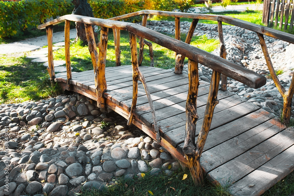 A small decorative wooden bridge in the summer park is built over a dried-up stream. Lawn design ideas and landscape design.