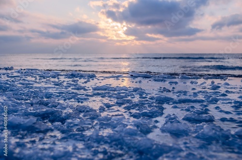 The frozen shore is covered with ice on the background of the sunset by the sea. Cold natural background