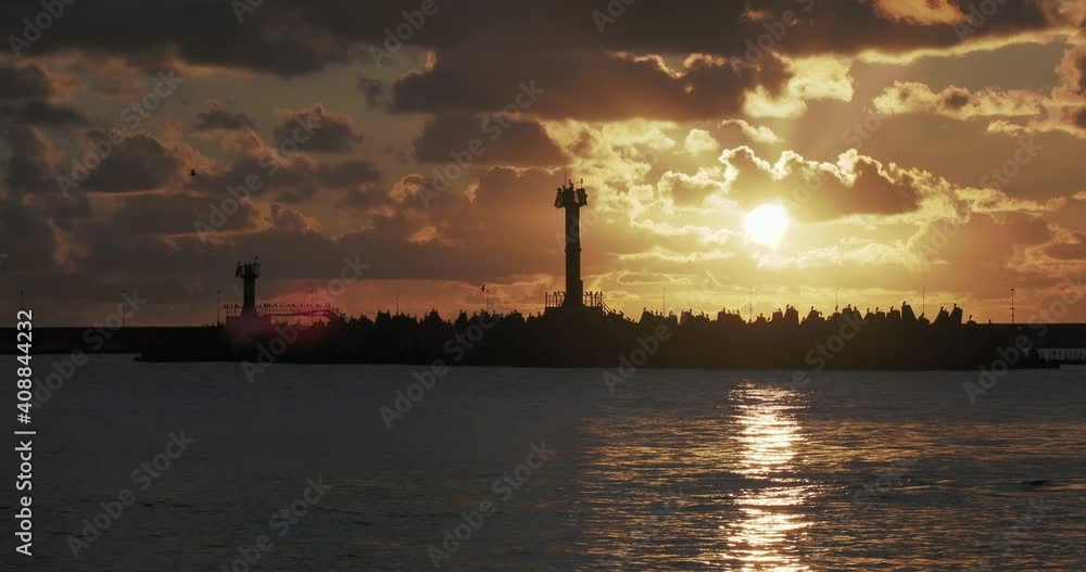Seagulls and cormorants sit on breakwater. Lighthouse on gorgeous sunset background. Port of Sochi, Russia.