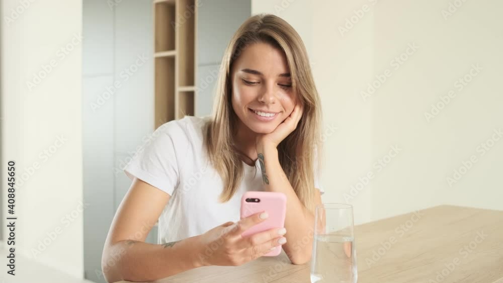 A beautiful woman is using her smartphone sitting at the table at home A beautiful woman is using her smartphone sitting at the table at home
