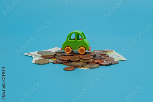 Green mini toy car on coins and banknotes on blue background. Buying car concept with copy space