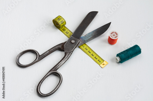 tailor scissors, spools of thread and a yellow centimeter on white background