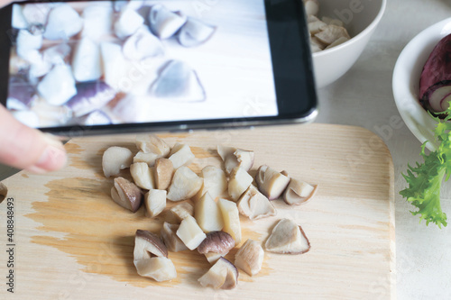 A woman photographs porcini mushrooms on a wooden board in her kitchen. Food blogger. Social media concept. Horizontal orientation.