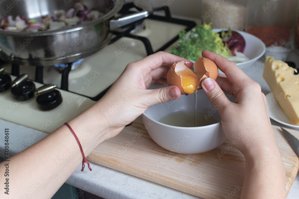 A woman holds a broken egg over a bowl in her kitchen. Food blogger. Social media concept. Horizontal orientation. A woman holds a broken egg over a bowl in her kitchen. Food blogger. Social media concept. Horizontal orientation.