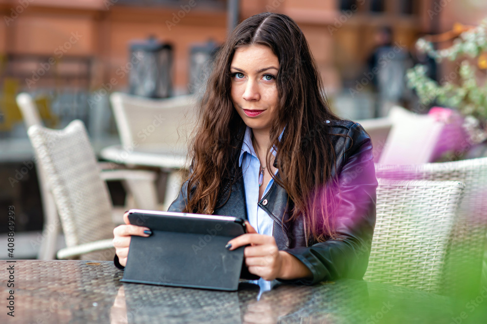 Fototapeta premium positive young female in casual clothes sitting in street cafe while working on remote project on digital tablet