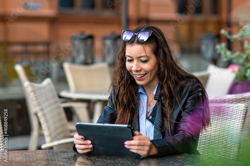 positive young female in casual clothes sitting in street cafe while working on remote project on digital tablet