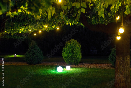 illumination park light garden with electric ground ball lantern with stone mulch and thuja bushes in outdoor landscaped park with garland of warm light bulbs, illuminate evening scene nobody.