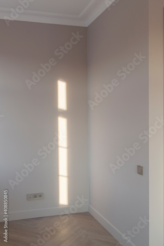 Close up view of modern and bright corner of empty cream room with ray of sunlight on wall and herringbone parquet floor