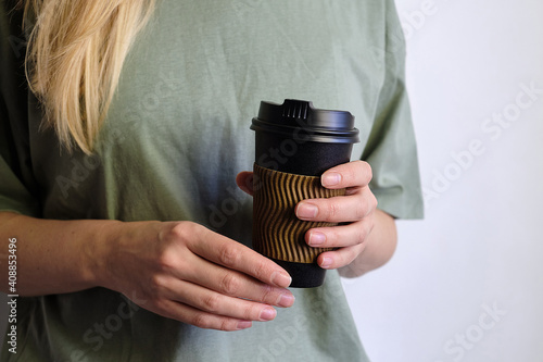 Woman holding in hand black paper cup with coffee or tea. Drink coffee time. Disposable paper cup. Beautiful blond hair young girl. Casual style, shirt and jeans. Take away. Hot beverage. Blank space