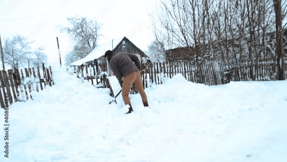 Man cleans snow with a shovel in the village in winter Man cleans snow with a shovel in the village in winter